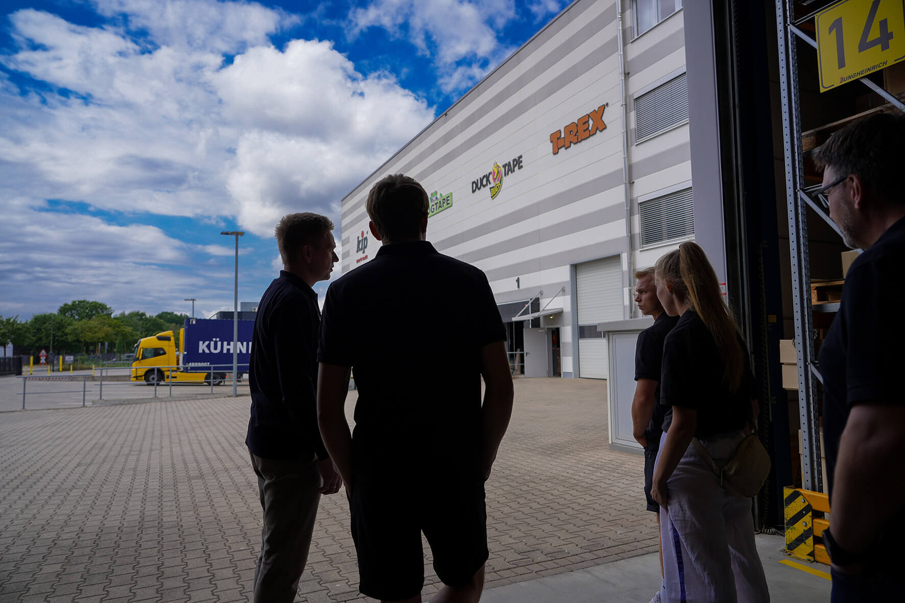 Das Maler Team Germany und Vertreter von Kip betrachten während eines Rundgangs über das Firmengelände in Bocholt den Außenbereich des Unternehmens vom Eingang einer Lagerhalle aus.